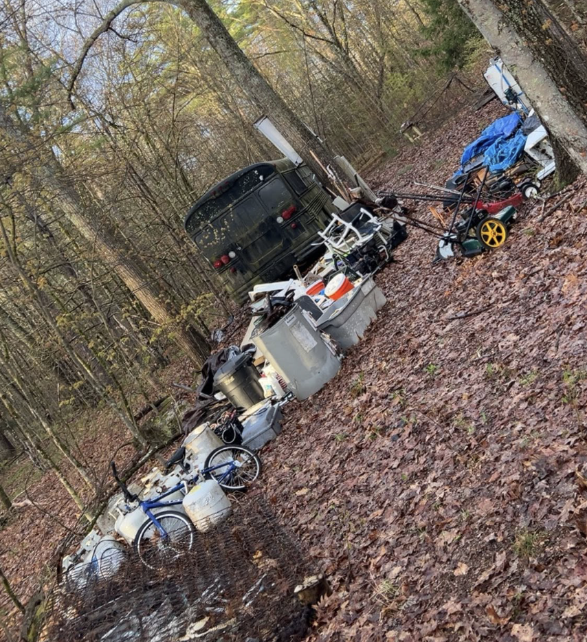Wooded area before junk removal with bins, scrap, and scattered debris.